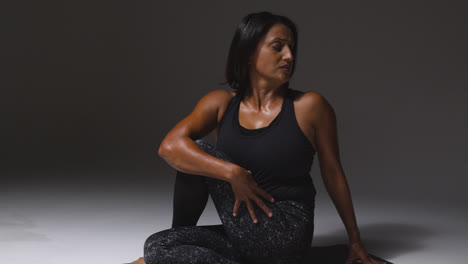 Foto-De-Estudio-De-Una-Mujer-Madura-Con-Ropa-De-Gimnasio-Sentada-En-El-Suelo-Haciendo-Ejercicios-De-Estiramiento-De-Pilates